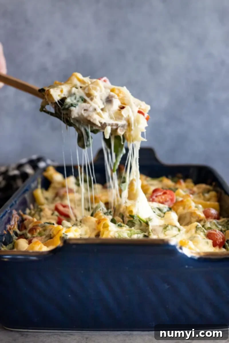 A serving spoon lifting a generous portion of Chicken Florentine Pasta Casserole from the dish, beautifully showcasing a long, stretchy cheese pull and the creamy, rich texture of the pasta, chicken, and spinach.