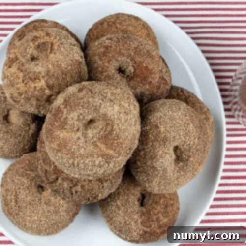 Apple cider donuts on a white platter with a cup of apple cider on the side.