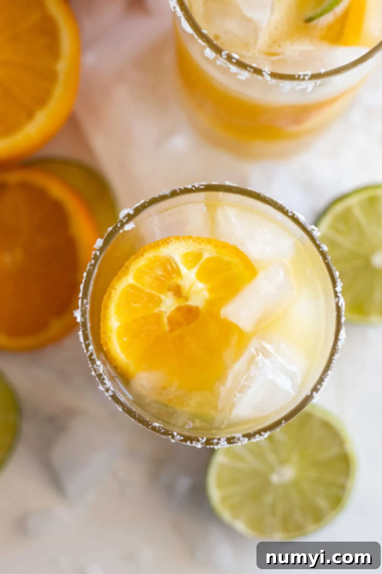 Zesty Orange Margarita 6 Overhead shot of the margarita in a glass. Sliced oranges and limes with crushed ice all around.