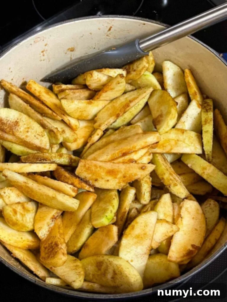 Slices of apples tossed with sugar and aromatic spices for apple pie in a large dutch oven.