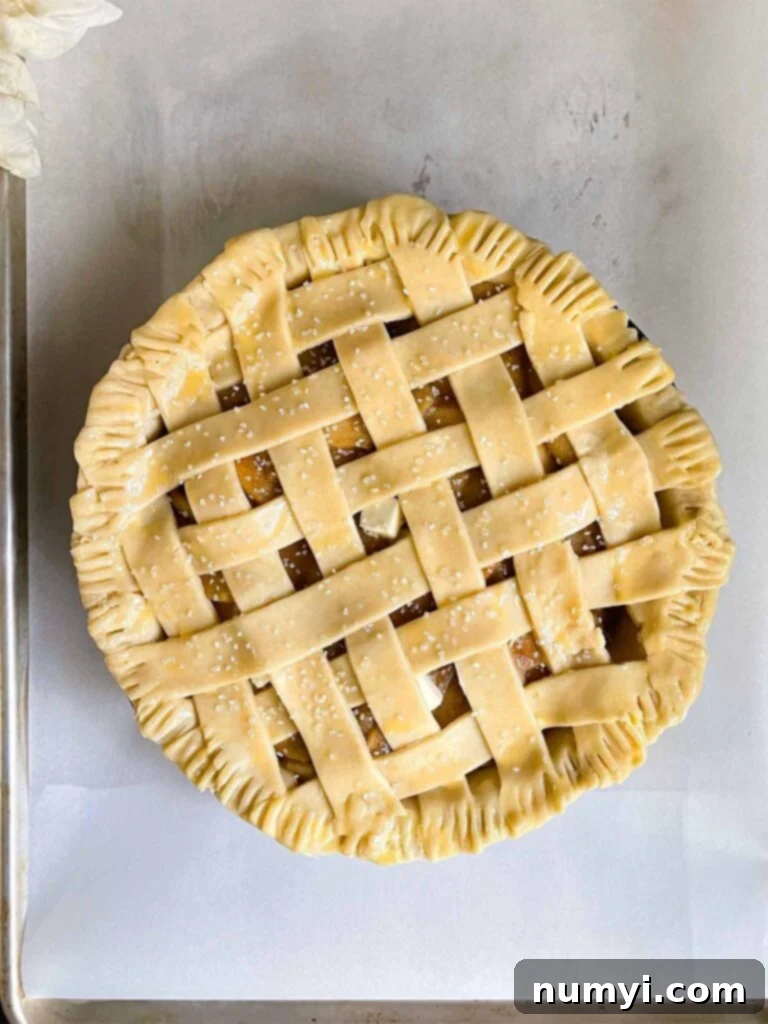 An unbaked lattice crust apple pie, ready for the oven, resting on parchment paper on a baking sheet.