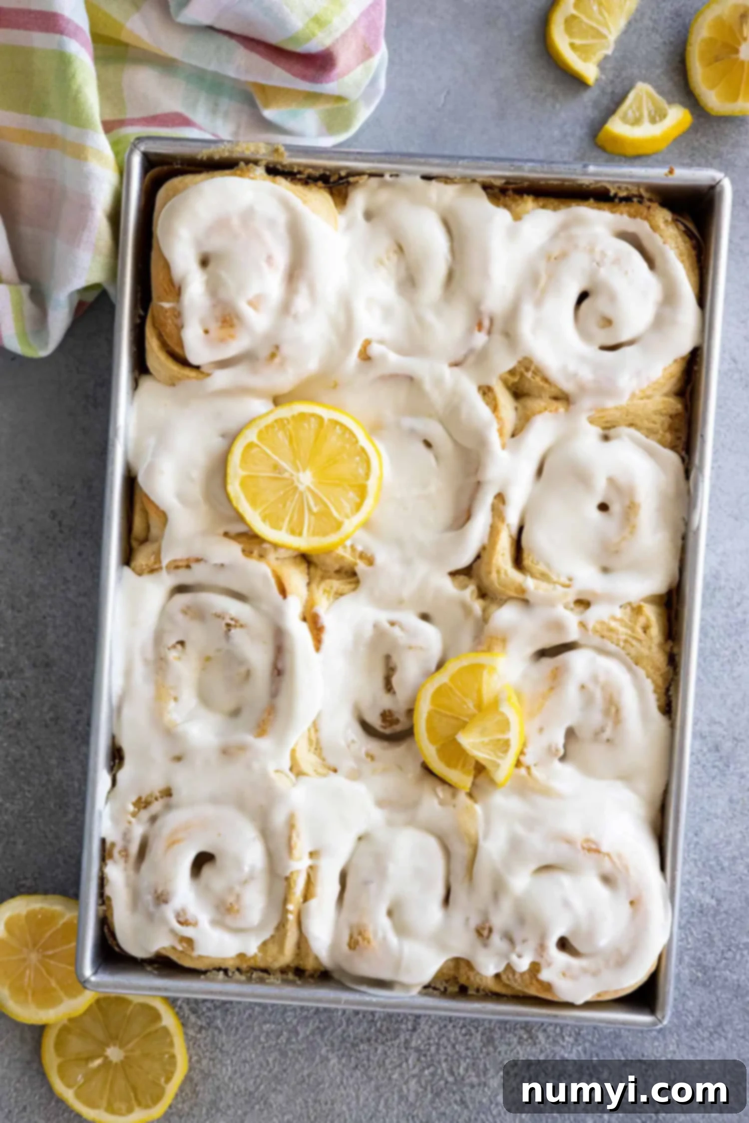 Overhead view of a pan of lemon sweet rolls topped with a cream cheese frosting and garnished with a few lemon slices. 