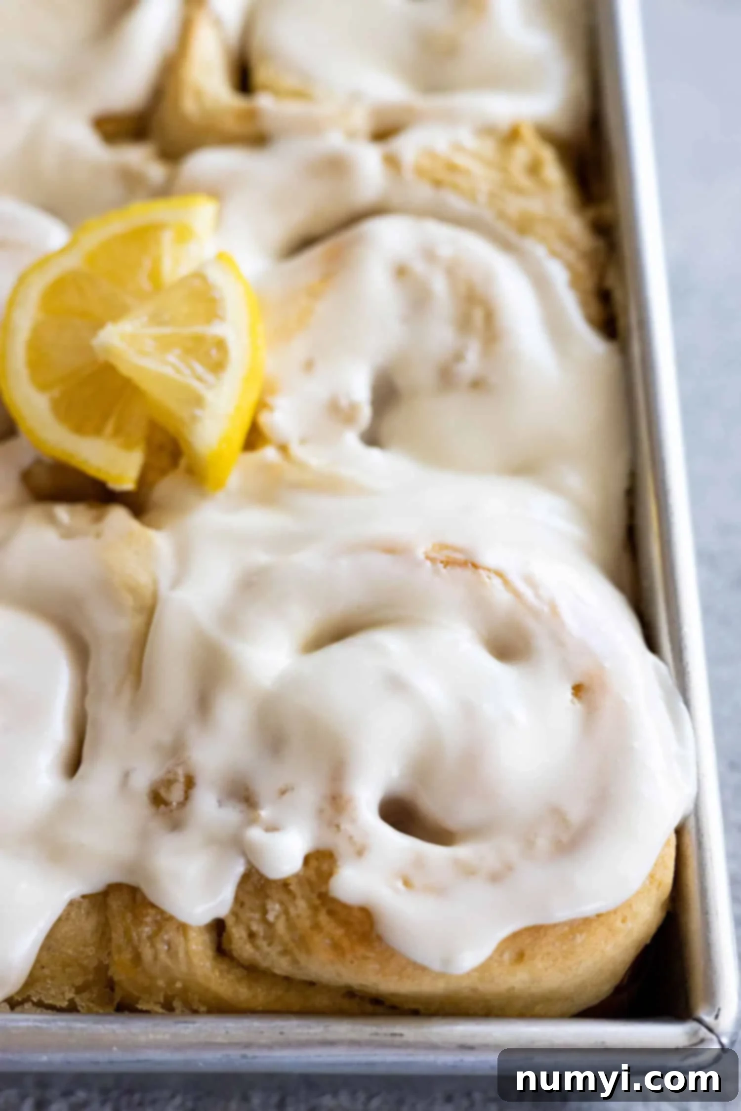 Close up of lemon sweet rolls in a pan topped with cream cheese frosting. 
