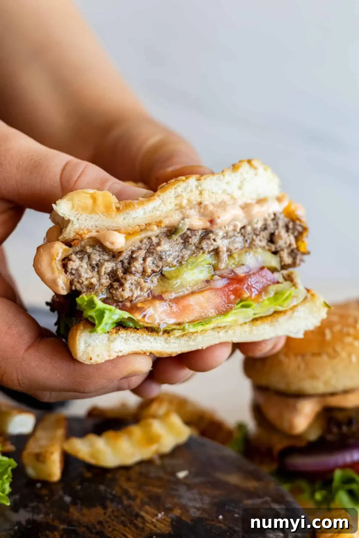 Two hands holding a burger cut in half, showcasing its juicy, slightly pink interior, perfectly melted cheese, and fresh toppings. This image emphasizes the deliciousness and perfect doneness of the burger.