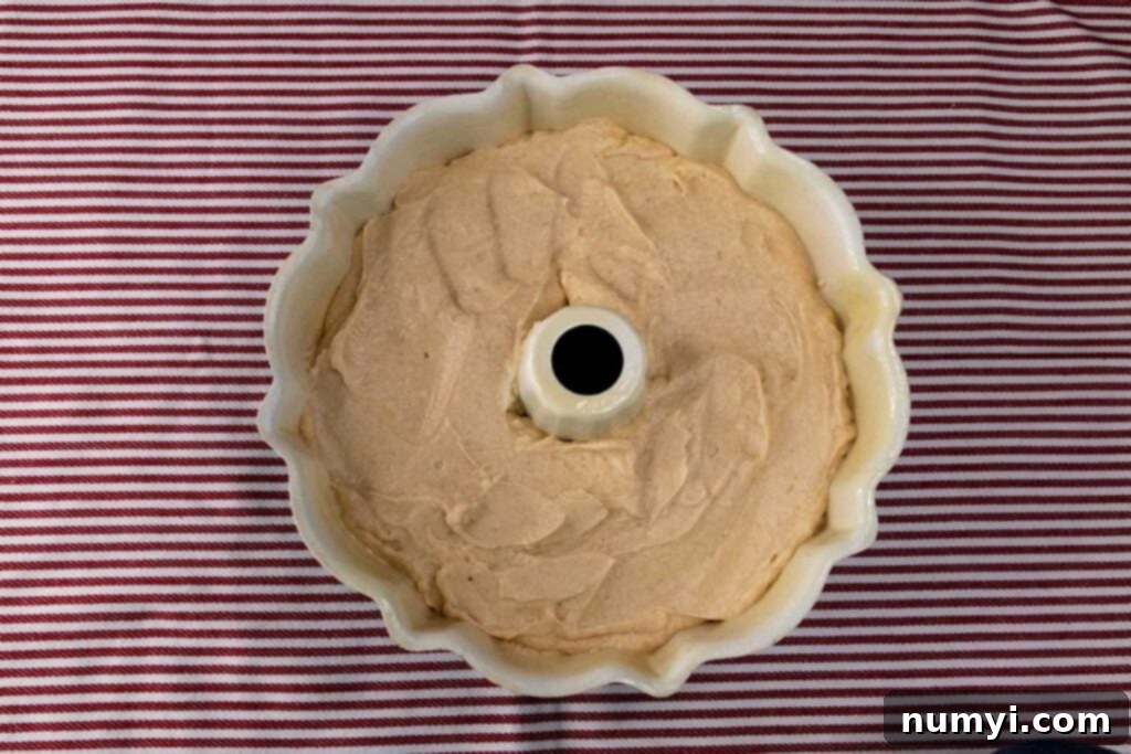 Raw apple cider pound cake batter smoothed into a classic bundt pan, ready for baking.