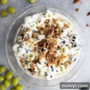 Overhead view of creamy grape salad in a bowl garnished with chopped nuts and brown sugar. Grapes and nuts sprinkled around the bowl.