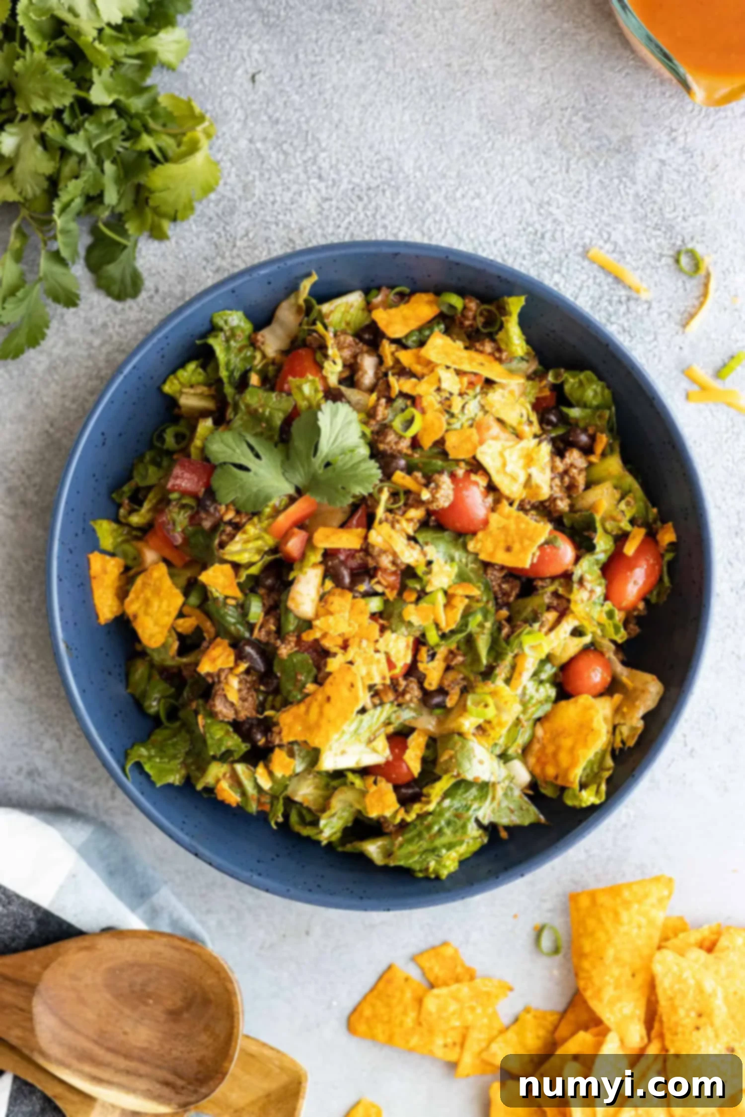 Overhead view of taco salad in a blue bowl with cilantro and chips off to the sides.