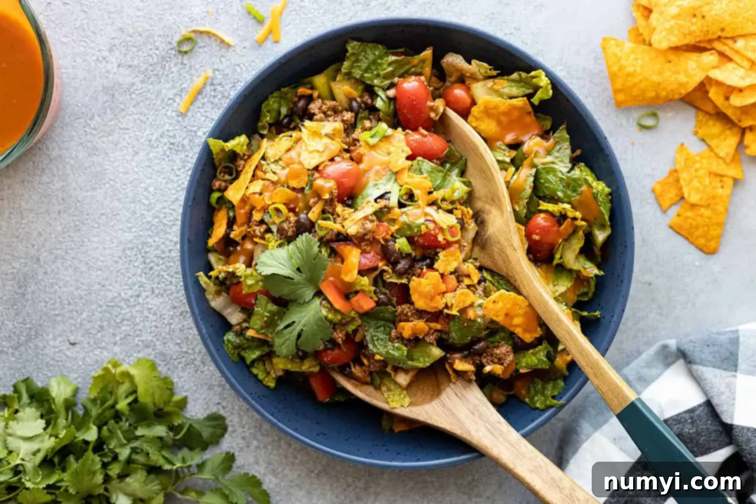 Overhead view of dorito taco salad in a blue bowl with serving utensils getting ready to serve the salad. 