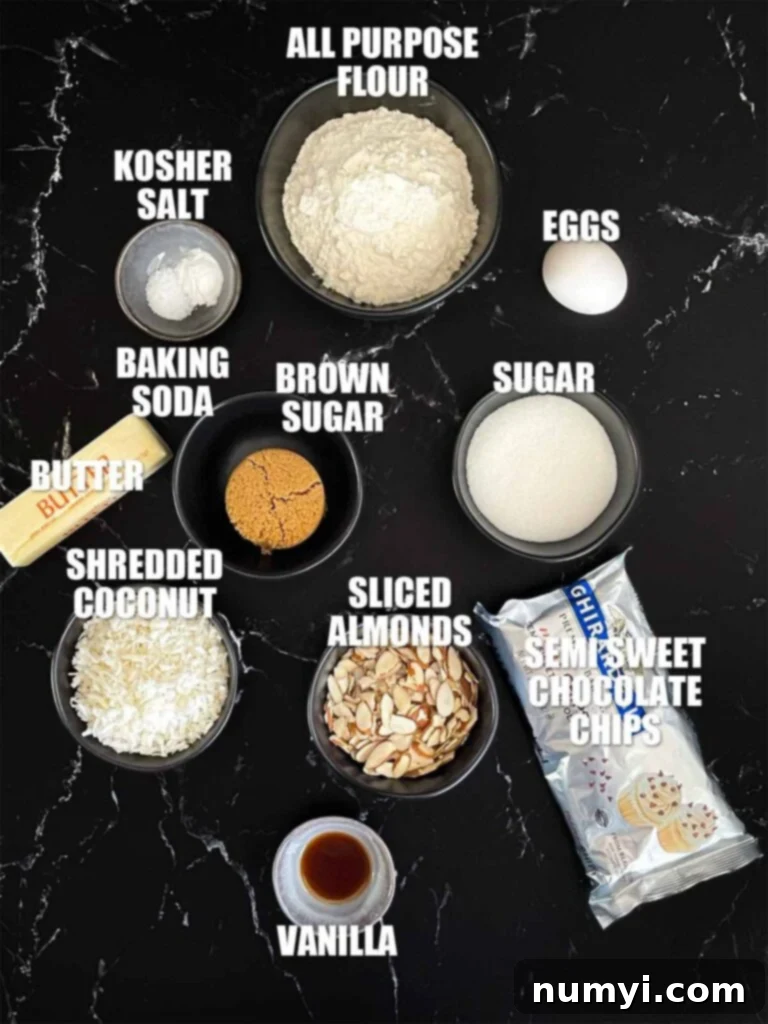 Almond joy cookies recipe ingredients laid out on a dark surface, including flour, sugars, butter, egg, vanilla, coconut, chocolate chips, and almonds.
