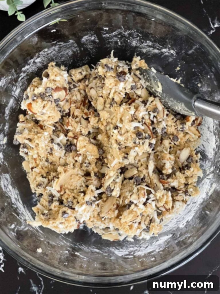 Almond joy cookie dough batter with all the add-ins – almonds, coconut flakes, and mini semi-sweet chocolate chips – perfectly mixed in a glass bowl.