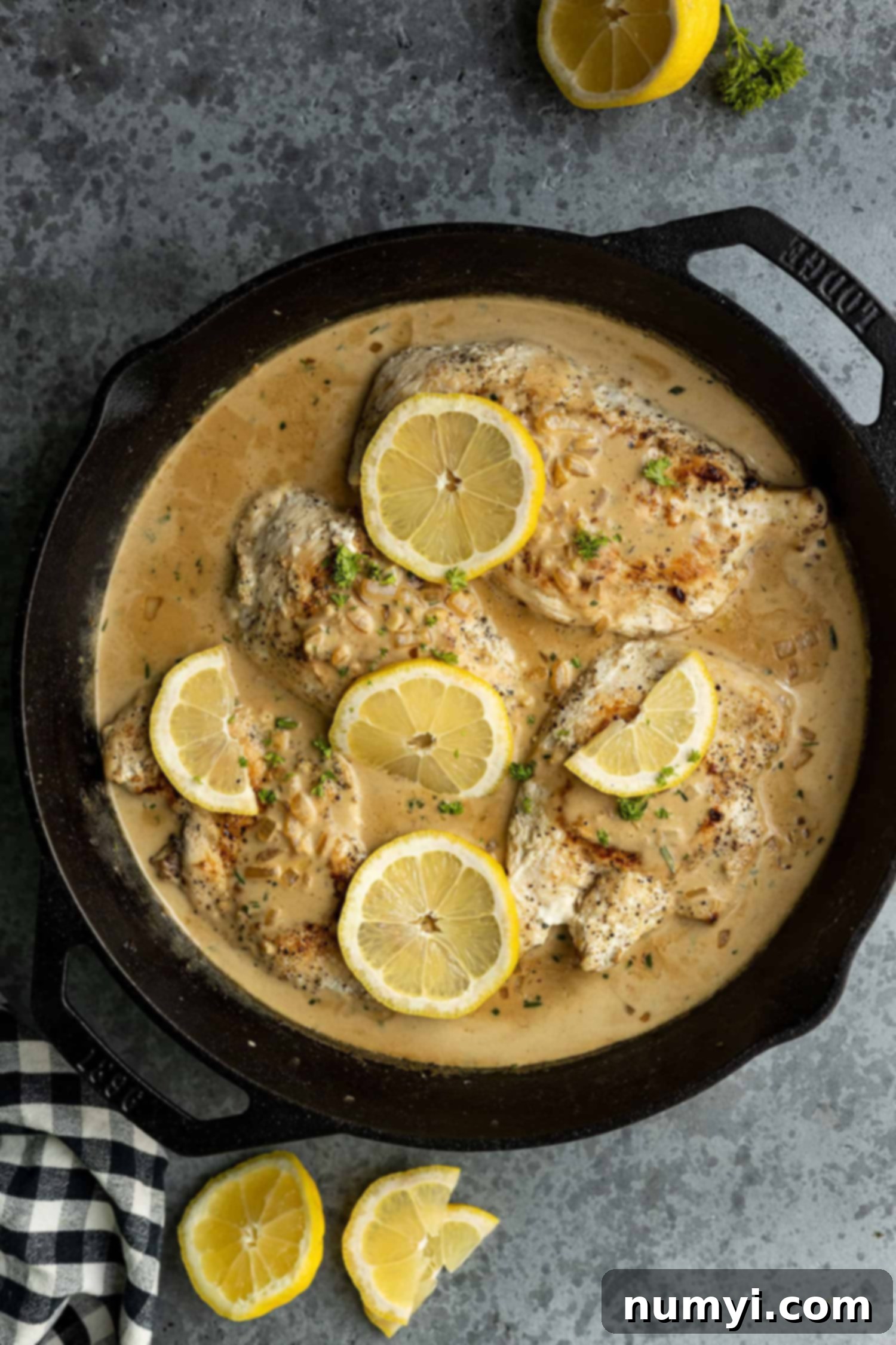 Overhead view of creamy lemon chicken in a cast iron skillet garnished with fresh lemon slices and vibrant parsley, ready to serve.