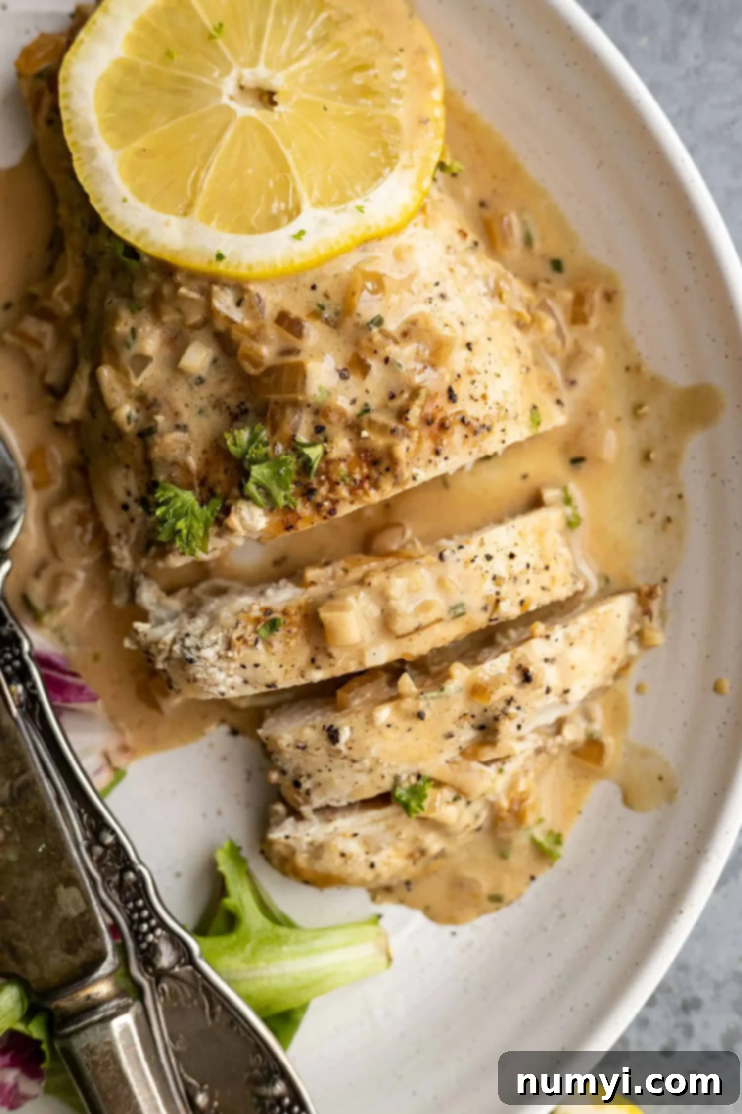 Overhead view of creamy lemon chicken sliced on a plate, generously drizzled with sauce and garnished with fresh parsley.