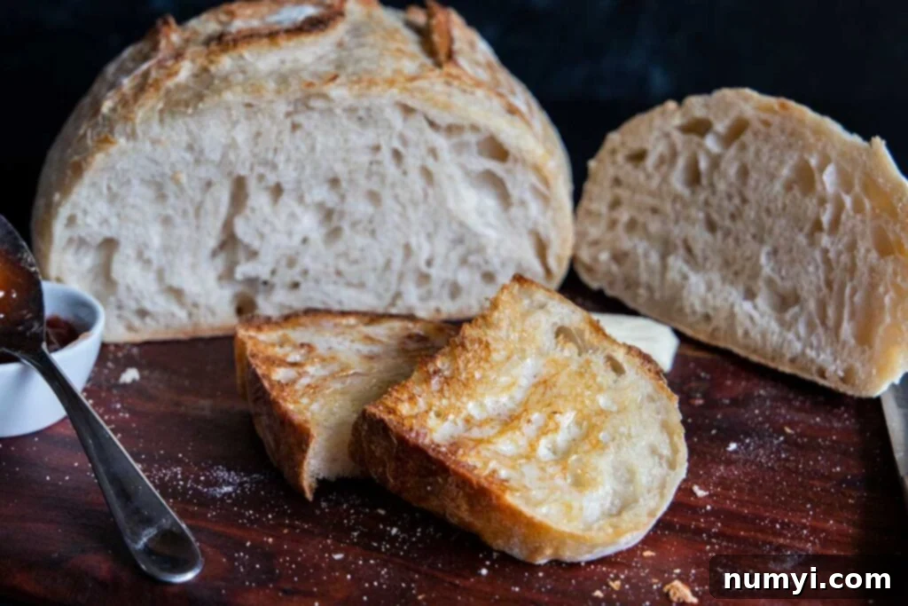 A delightful sourdough batard on a cutting board, accompanied by a piece of perfectly buttered sourdough toast.