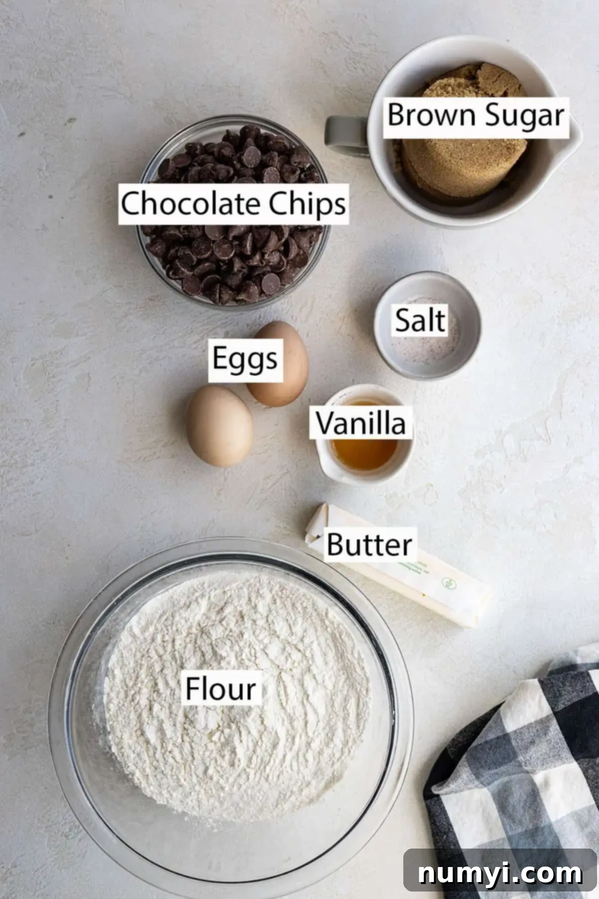 A flat lay photograph showcasing the essential ingredients for chocolate chip cookie bars: dark brown sugar, various chocolate chips, fresh eggs, vanilla extract, a pinch of salt, melted butter, and all-purpose flour.