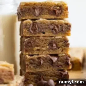 Tall stack of golden brown chocolate chip cookie bars next to a tall glass of milk, ready to be enjoyed.
