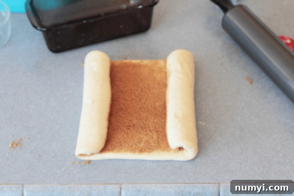 The process of rolling cinnamon sugar into bread dough, showing the sweet filling spread evenly before shaping.