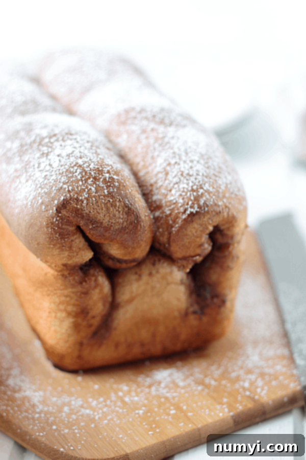 A rustic, whole loaf of Cinnamon Swirl Bread generously dusted with powdered sugar, ready to be sliced and enjoyed.