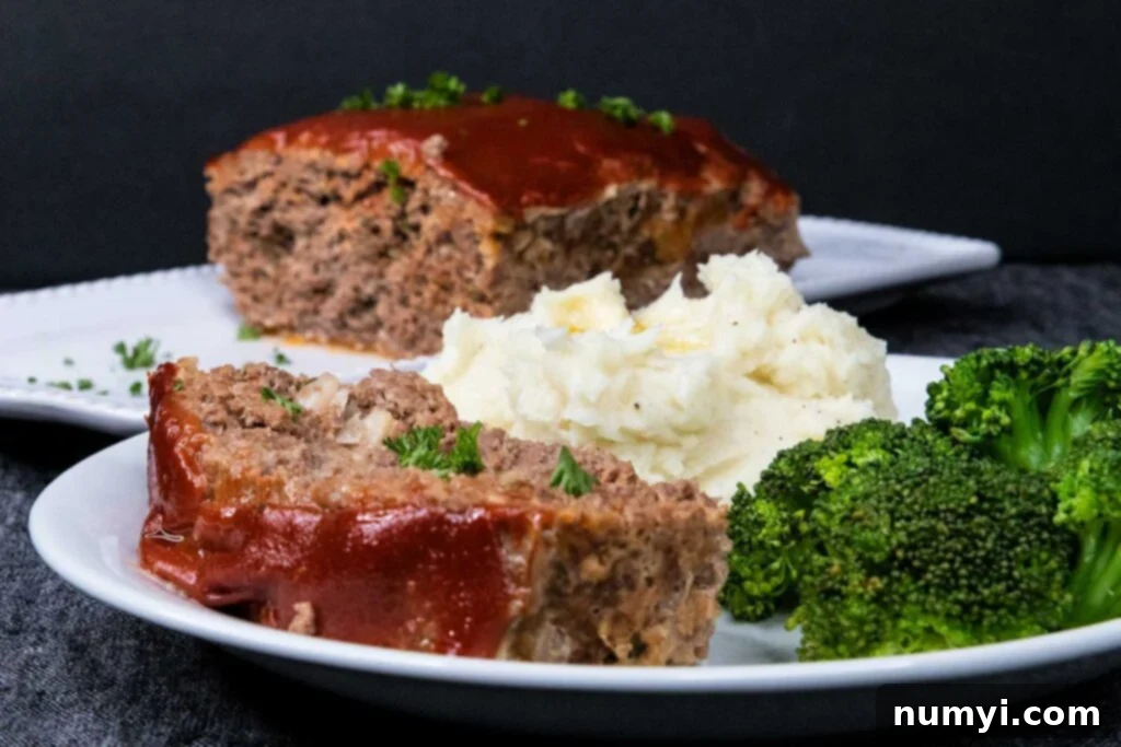 Effortless Weeknight Meatloaf 2 A generous slice of homemade meatloaf served with creamy mashed potatoes and vibrant green broccoli florets on a pristine white plate, garnished with fresh herbs.
