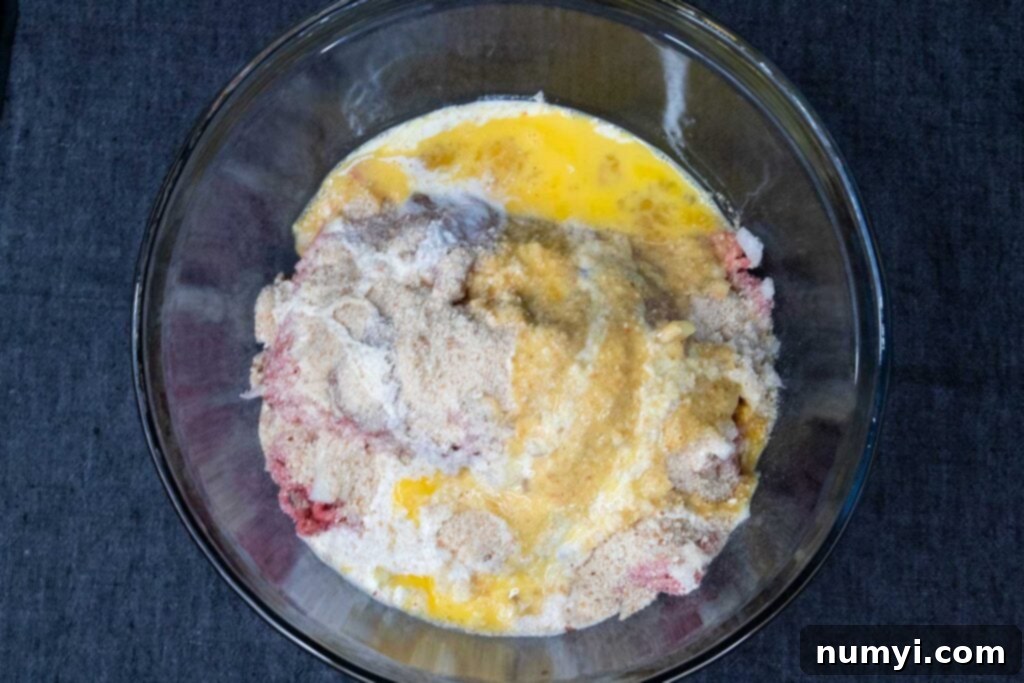 Effortless Weeknight Meatloaf 3 Various raw meatloaf ingredients, including ground beef, chopped onions, and spices, neatly arranged in a clear glass mixing bowl before combining.