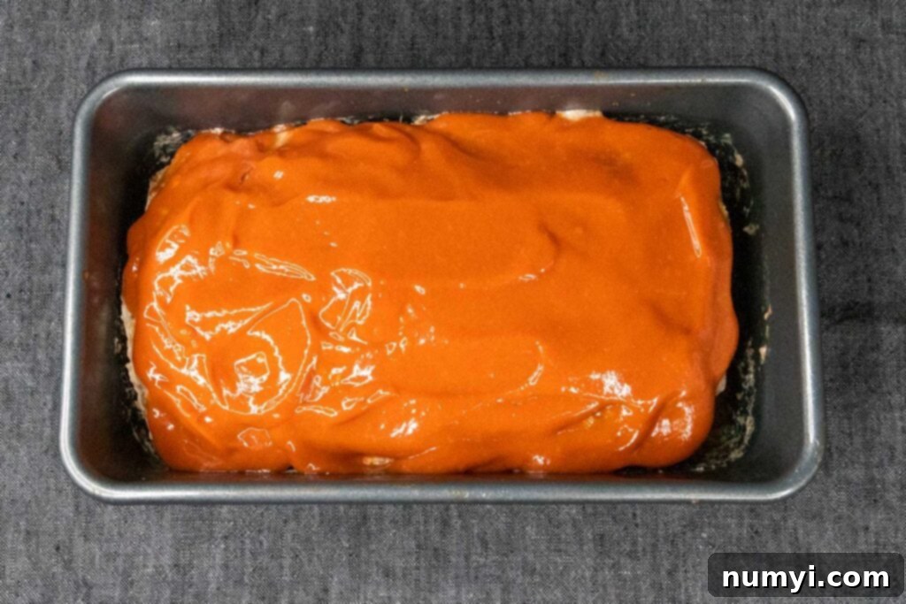 Effortless Weeknight Meatloaf 5 Partially baked meatloaf generously covered with a rich, red homemade ketchup glaze in a loaf pan, ready for the final baking stage.