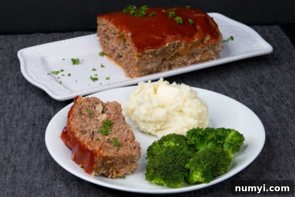 Effortless Weeknight Meatloaf 6 A perfectly cooked slice of classic meatloaf, accompanied by a generous serving of creamy mashed potatoes and vibrant green steamed broccoli, resting on a white dinner plate.