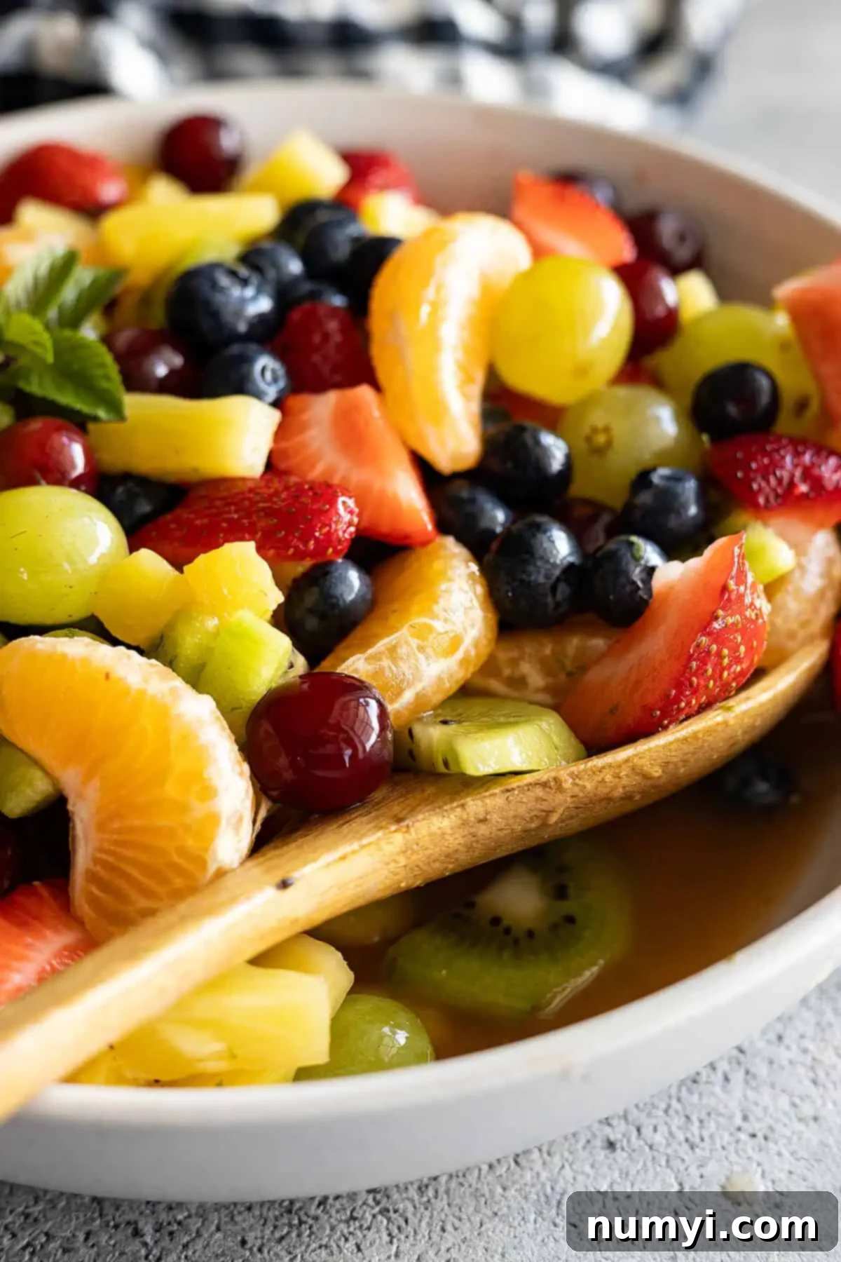 Fruit salad in a cream bowl with spoon off to the side ready to scoop up some fruit salad.