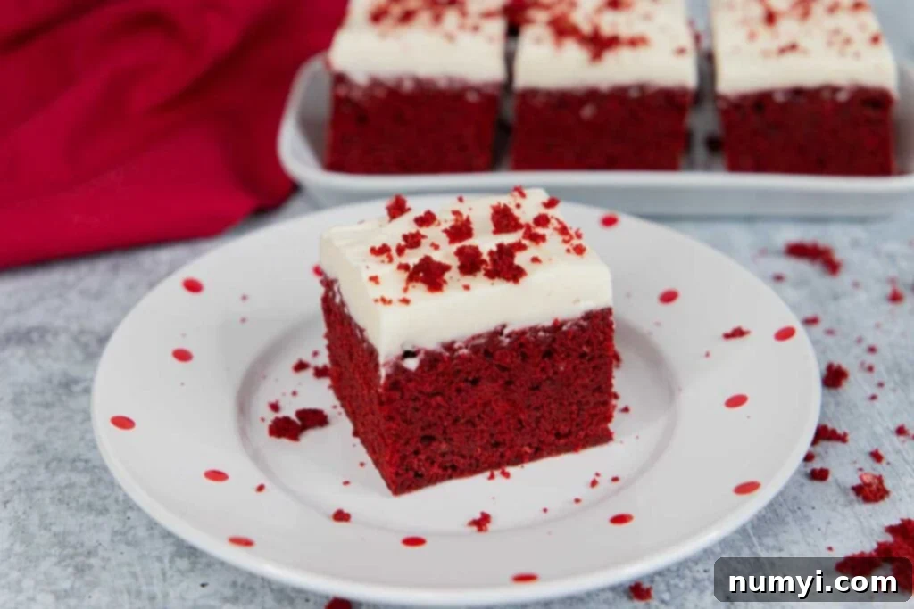 Red velvet brownie square with cream cheese frosting, garnished with brownie crumbs on a light plate with red dots.
