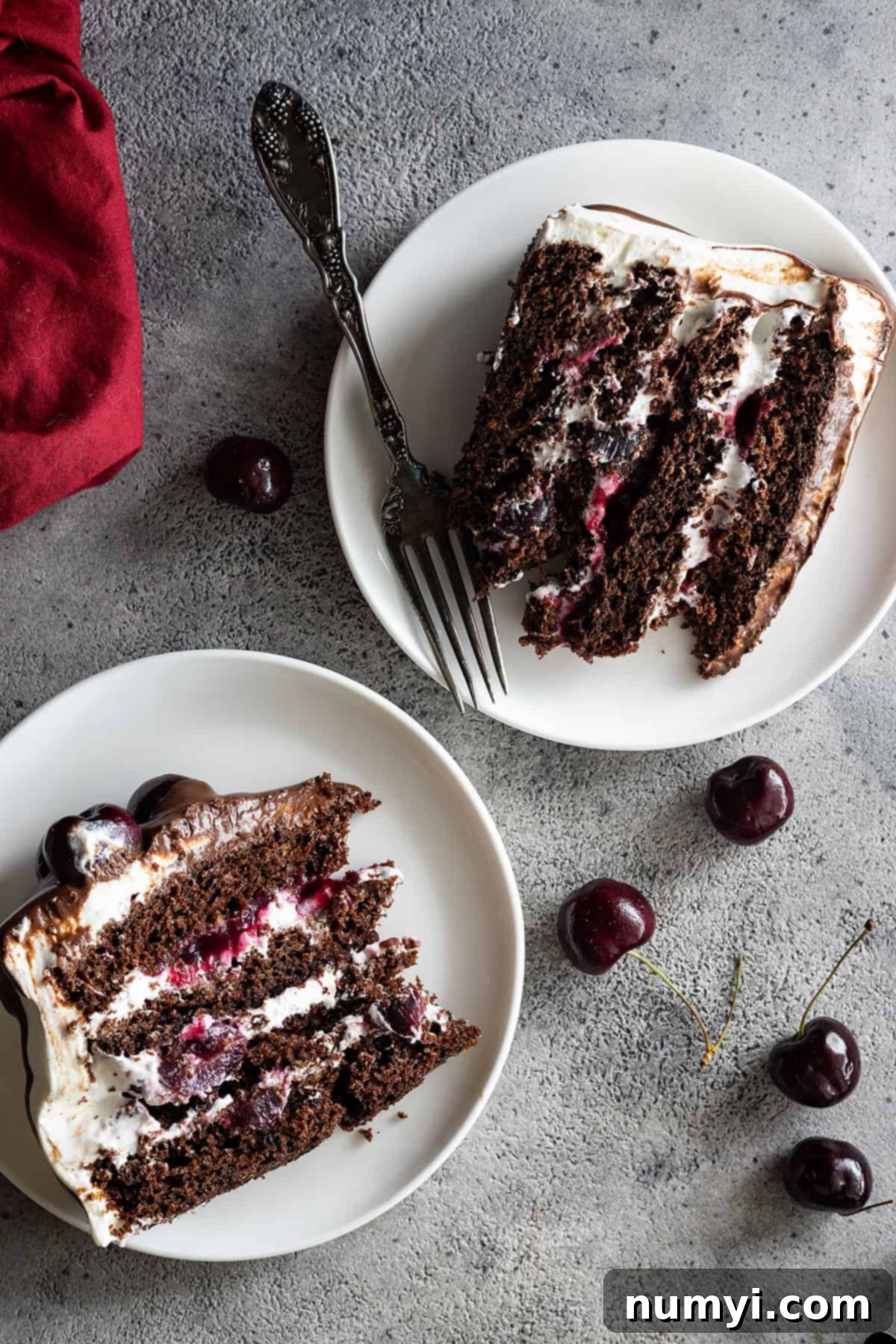Overhead view of 2 slices of cake on white plates with red napkin off to the side. 