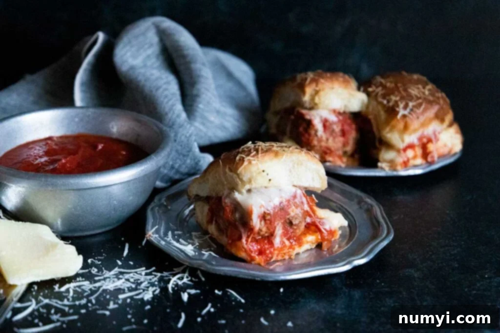 Meatball sliders on a silver plate garnished with shaved parmesan cheese.