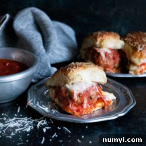 Meatball sliders on a silver plate garnished with shaved parmesan cheese.