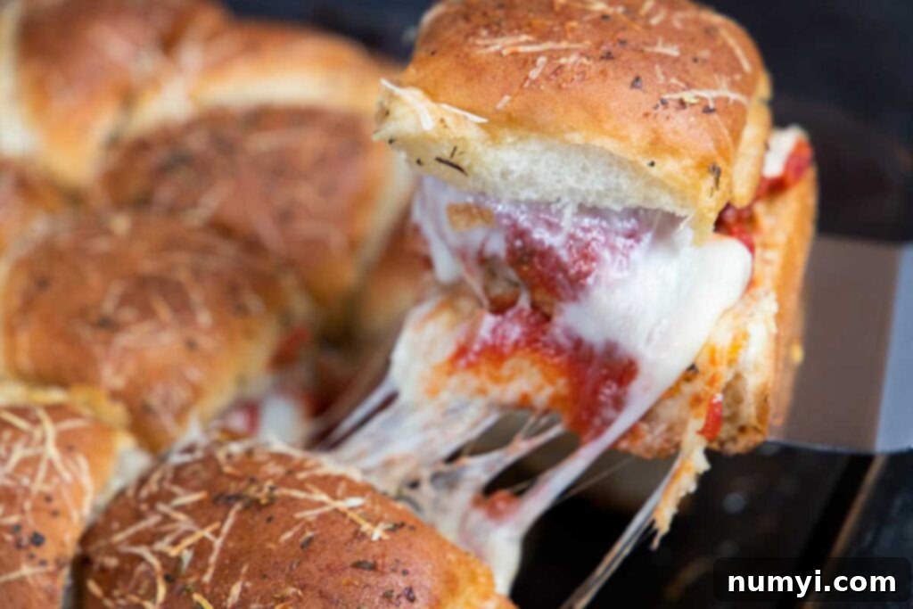 A meatball slider being removed from the 9x13 inch baking dish.