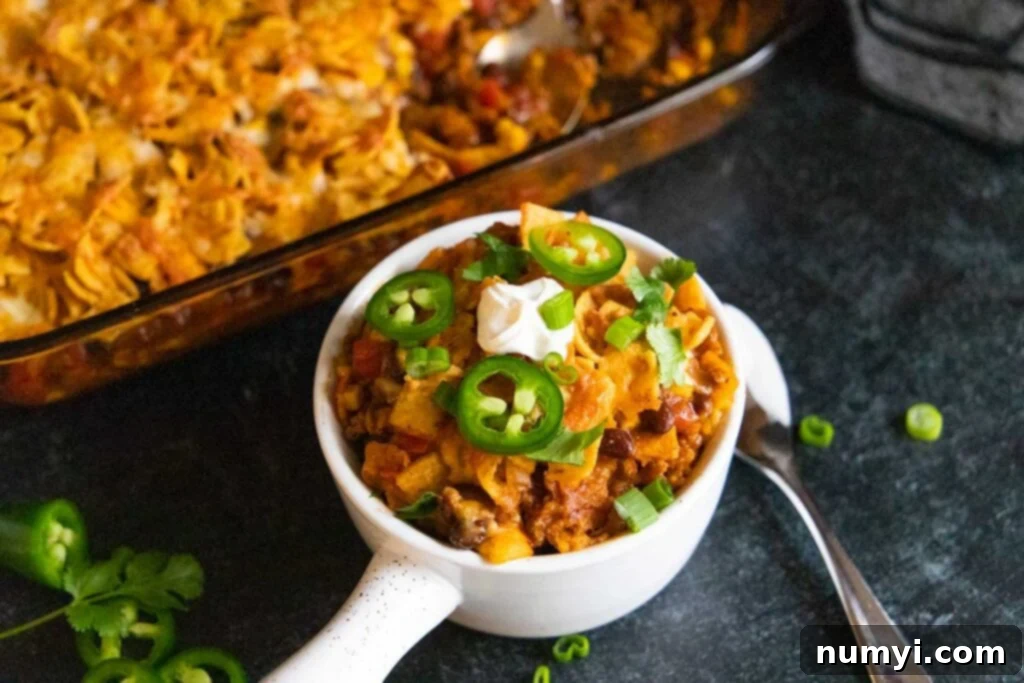 Frito pie casserole in a white bowl, garnished with fresh herbs.