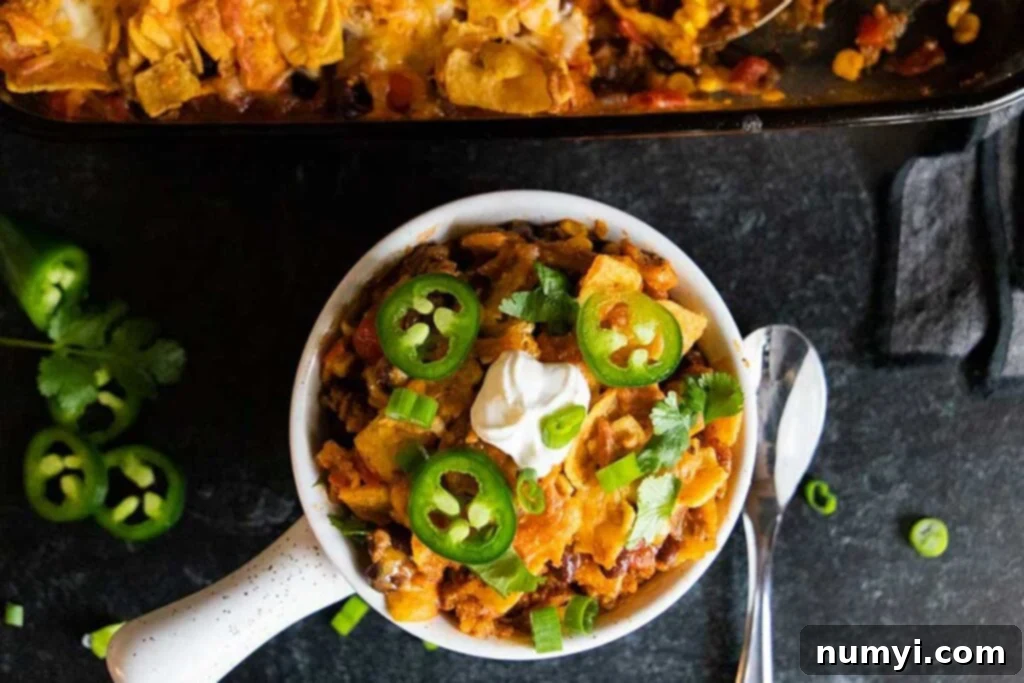 Frito pie casserole in a white bowl with various toppings.
