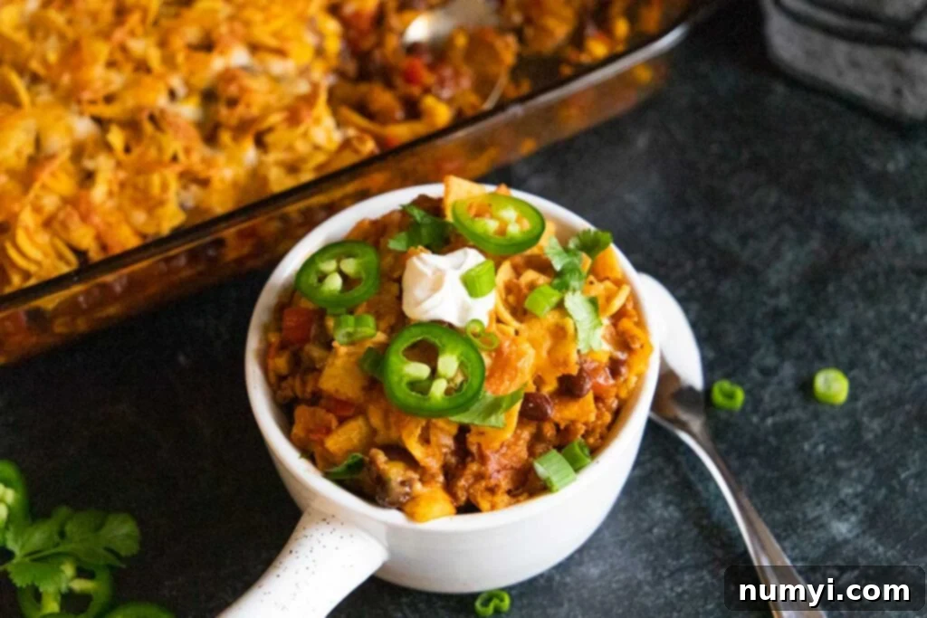 Frito pie casserole in a white bowl, garnished and ready for serving.