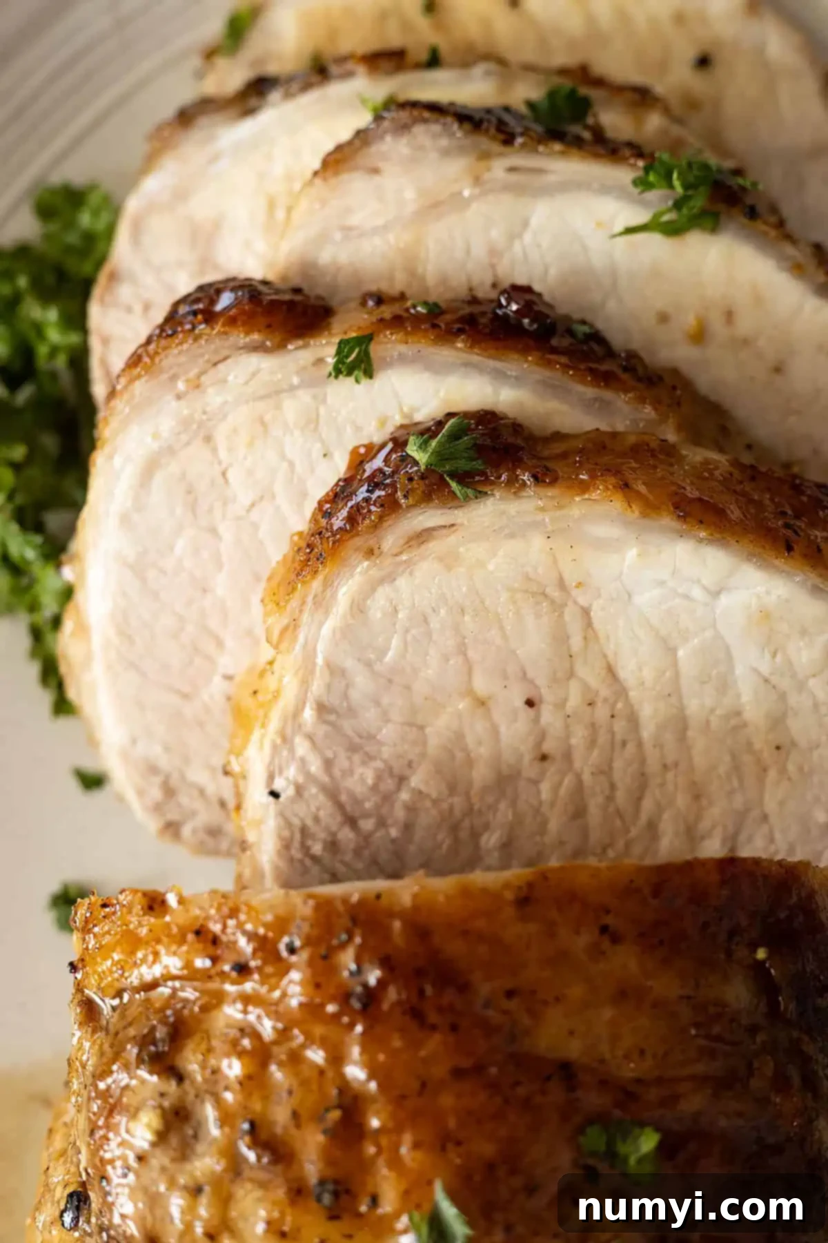 A close-up of tender, juicy slices of maple glazed pork loin, beautifully garnished with fresh parsley.