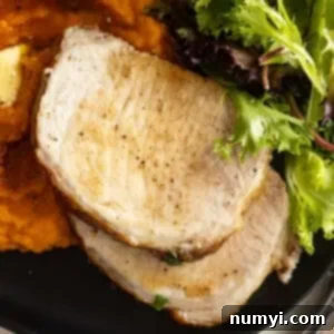 Overhead of sliced pork on a black plate with mashed sweet potatoes and a salad.