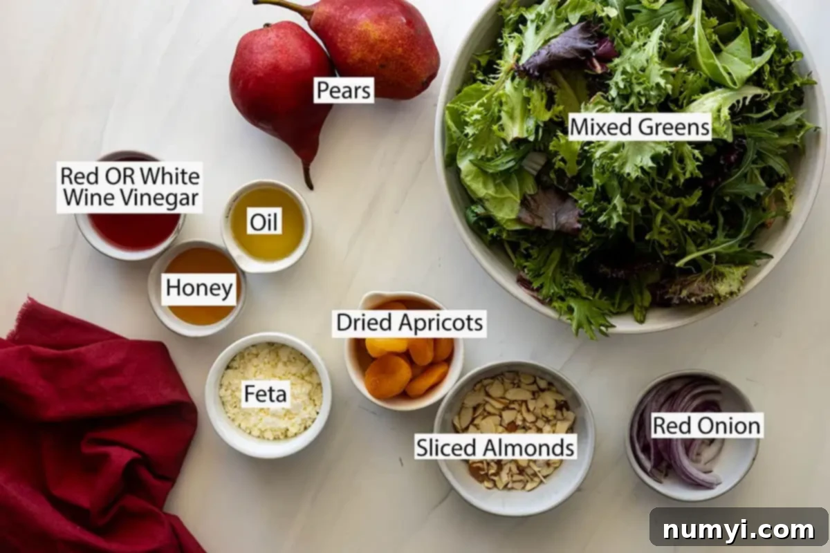 Ingredients for Pear Salad with Apricots laid out: Mixed greens, fresh pear, dried apricots, crumbled feta cheese, sliced almonds, red onion, white or red wine vinegar, honey, and neutral oil.