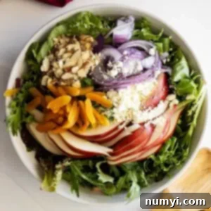 Overhead view of salad ingredients in a large white bowl. Salad tongs and red napkin off to the side.