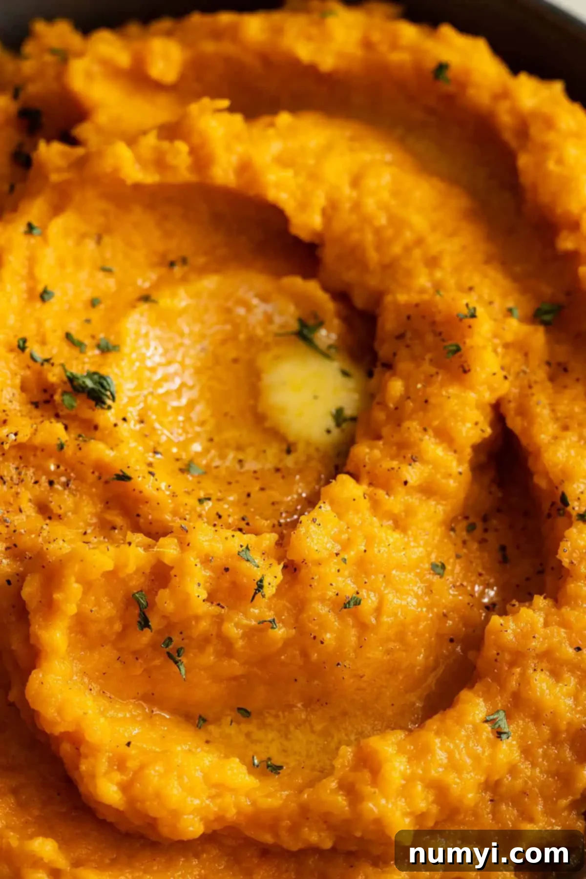 Velvety Sweet Potato Mash 7 Close up of mashed sweet potatoes with pools of melted butter, fresh black pepper, and parsley.