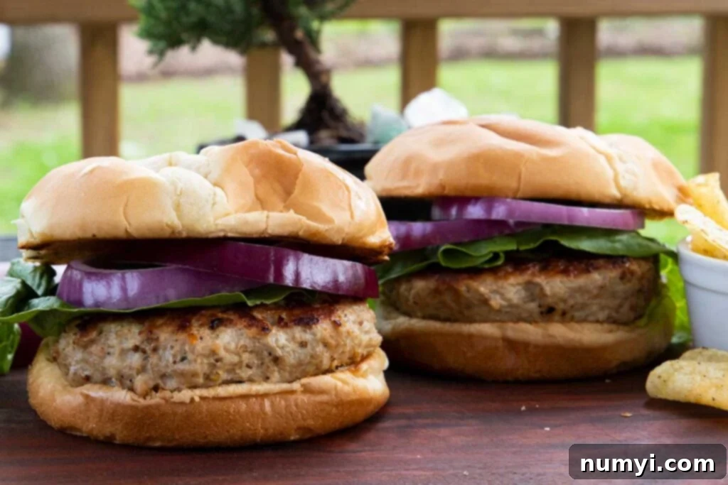 Two beautifully cooked turkey burgers, topped with fresh lettuce and vibrant red onion, ready to be placed on buns and enjoyed.
