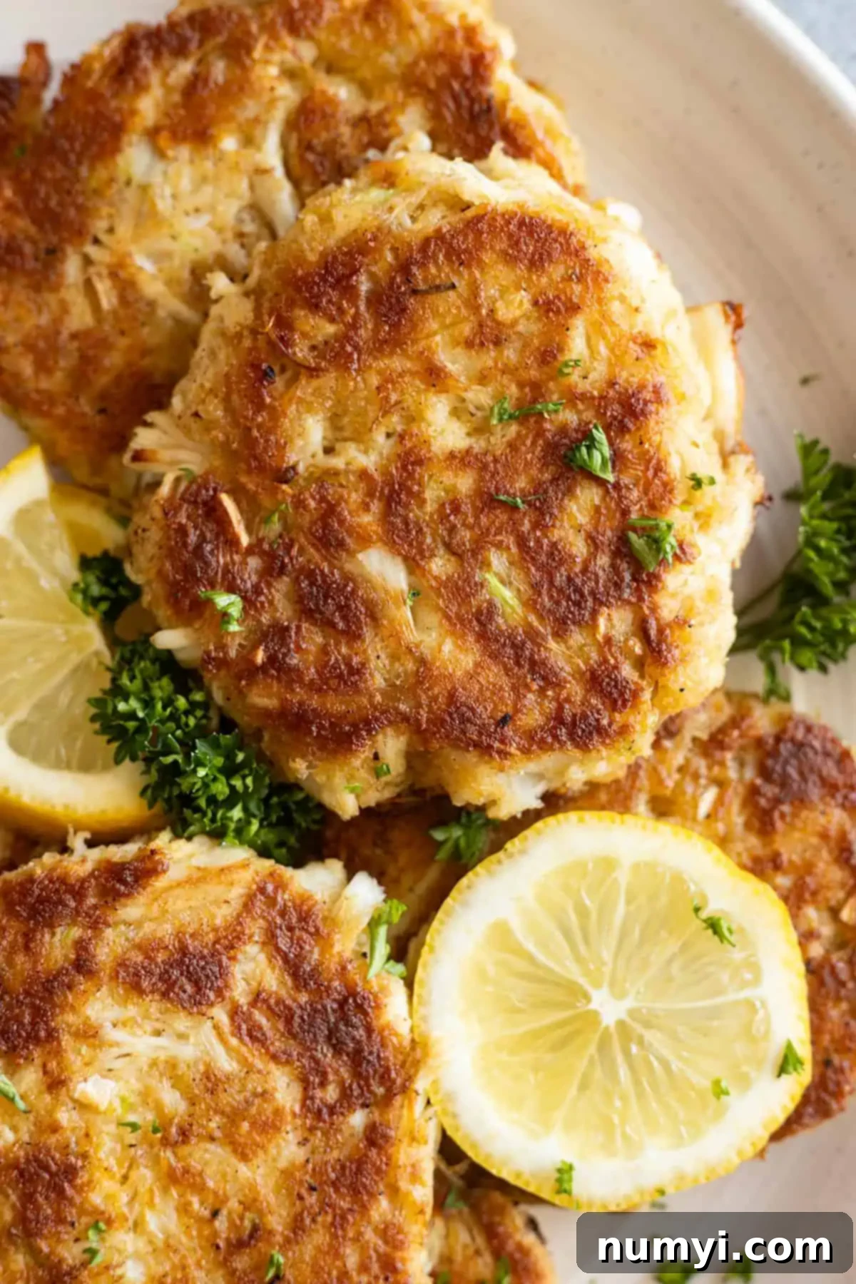 Simply Perfect Crab Cakes 5 Close up of cakes on a plate garnished with fresh lemon and parsley.