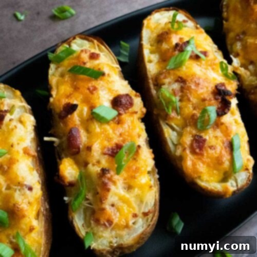Twice baked potatoes on an oval black platter garnished with diced green onions.