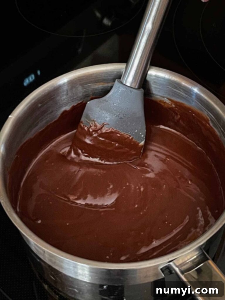 Dark chocolate chips being stirred into the boiled fudge ingredients in a metal saucepan, creating a rich chocolate mixture.