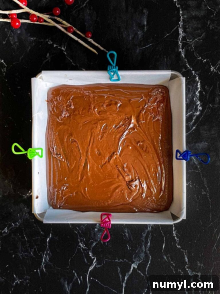Dark chocolate fudge poured into a baking pan lined with parchment paper, ready to set.