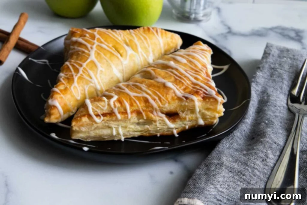 Quick & Flaky Apple Hand Pies 3 Puff pastry apple turnovers on a black plate.