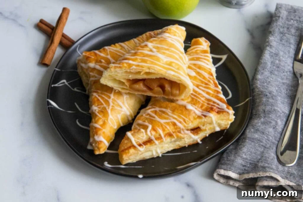 Quick & Flaky Apple Hand Pies 8 Puff pastry apple turnovers on a black plate with cinnamon sticks and apples as garnish.