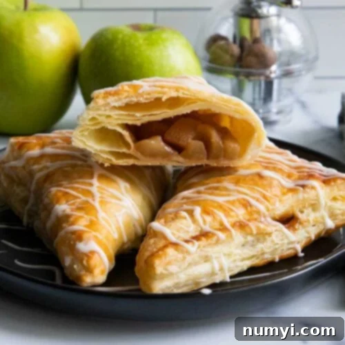 Quick & Flaky Apple Hand Pies 9 Apple turnovers on black plate with green apples in the background.