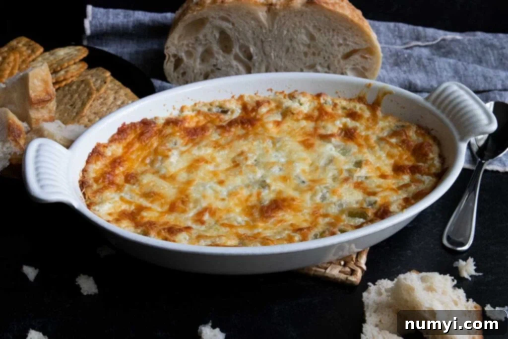 Artichoke dip in a white oval baking dish with bread in the background.