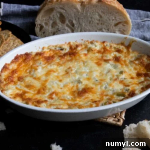 Artichoke dip in a white oval baking dish with bread in the background.