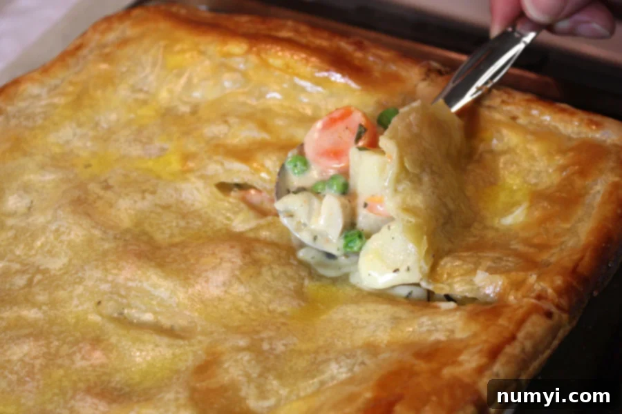 Homemade Chicken Pot Pie with a golden, flaky puff pastry crust and a spoon just breaking through the top, revealing the creamy chicken and vegetable filling.
